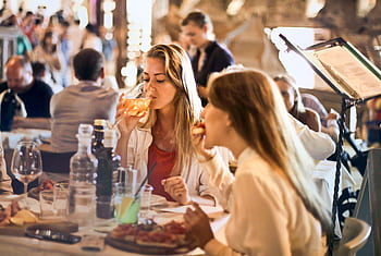 Friends dining in a cozy Italian restaurant, enjoying drinks and food in a lively atmosphere. HD wallpaper