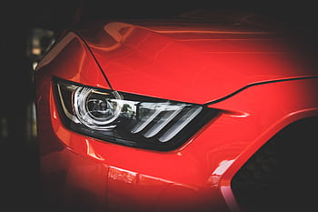 Detailed view of a red Ford Mustang's headlight showcasing sleek automotive design. HD wallpaper