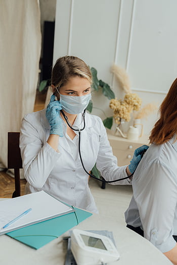 A healthcare professional in PPE using a stethoscope for a medical check-up. HD phone wallpaper