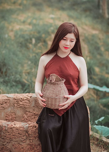 Asian woman sitting with a wicker basket in a peaceful outdoor setting, showcasing traditional attire. HD phone wallpaper