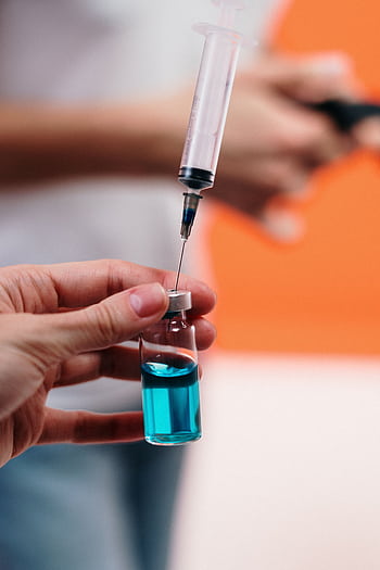 A syringe draws blue liquid from a vial, focusing on precision in healthcare. HD phone wallpaper