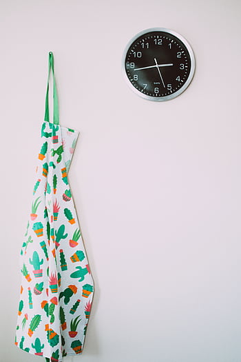 A minimalist kitchen wall featuring a colorful cactus-patterned apron and a modern clock. HD phone wallpaper
