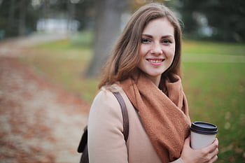 Portrait of a smiling woman holding a coffee cup in a serene autumn park setting. HD wallpaper