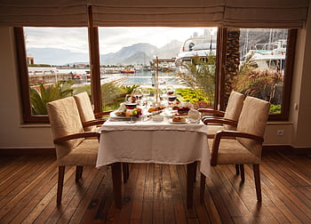 Elegantly set table in a seaside restaurant with a marina view, featuring gourmet dishes and fine dining setup. HD wallpaper