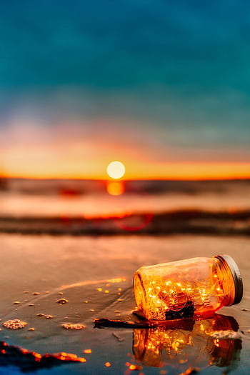 A lit jar with lights sits on a beach, creating a tranquil scene during sunset. HD phone wallpaper