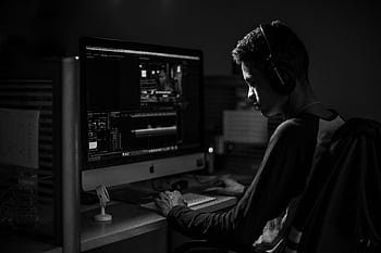 A man wearing heads working on video editing on a computer in a dimly lit office. HD wallpaper