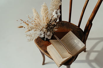 A dried flower bouquet and open book placed on a wooden chair, creating a rustic still life scene. HD wallpaper