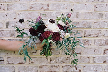 Chic floral bouquet with roses and greenery held against a rustic brick wall. HD wallpaper