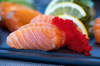 Close-up of fresh salmon sashimi topped with bright red caviar and garnished with lemon slices. HD wallpaper