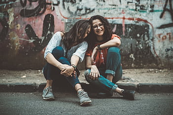 Two women laughing and enjoying each other's company on a graffitied street. HD wallpaper