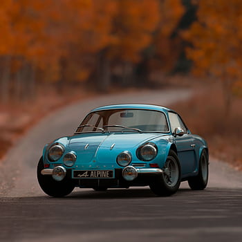 Classic Alpine A110 sports car driving on an autumn road with vibrant foliage. HD phone wallpaper