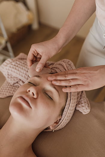 Woman enjoying a soothing facial massage with gua sha tool, promoting relaxation and skin care. HD phone wallpaper