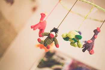 Colorful knitted animal toys hanging from a nursery mobile creating a playful atmosphere. HD wallpaper