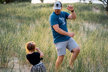 A father dances playfully with his daughter in a sunny field, capturing joy and bonding. HD wallpaper
