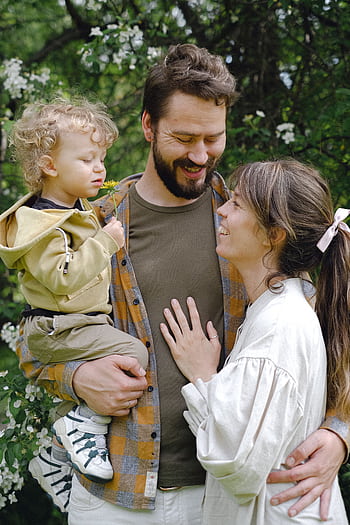 A joyful family moment captured in a Spring garden, featuring a child with parents embracing. HD phone wallpaper