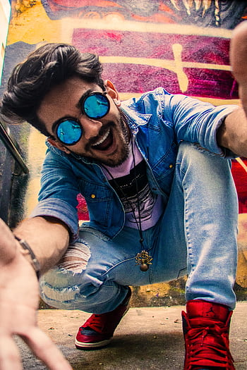 A lively portrait of a young man in urban streetwear, enjoying a vibrant city background. HD phone wallpaper