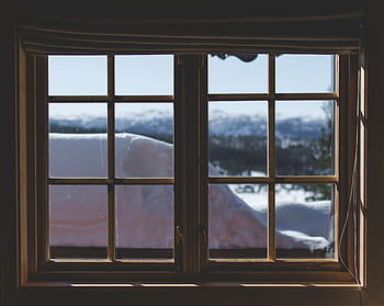 A scenic view of snow-capped mountains through a wooden window frame, capturing the serene winter landscape. HD wallpaper