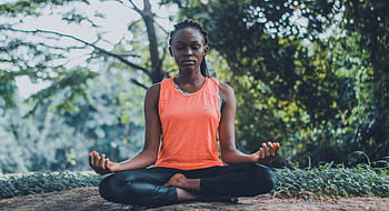A woman meditating peacefully outdoors in a lush green setting, promoting relaxation and mindfulness. HD wallpaper