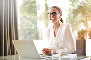 Cheerful businesswoman in glasses working on a laptop, in a bright and modern office setting. HD wallpaper