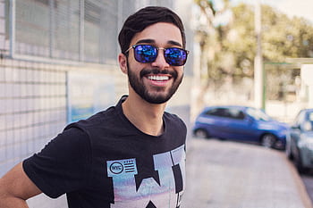 Portrait of a smiling man wearing sunglasses outdoors, showcasing modern fashion and style. HD wallpaper