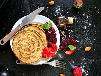 Top view of pancakes with strawberry jam, fresh strawberries, almonds, and honey on a dark kitchen counter. HD wallpaper
