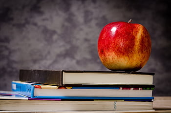 Red apple placed atop stacked books symbolizes education and learning. HD wallpaper