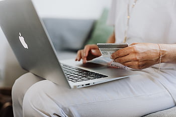 Close-up of a person holding a credit card while shopping online using a laptop at home. HD wallpaper