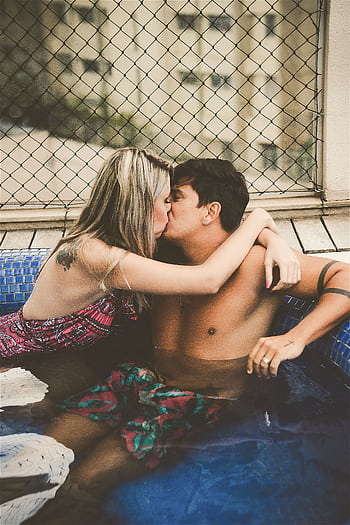 A loving couple sharing a romantic kiss in a rooftop pool, surrounded by a cityscape. HD phone wallpaper
