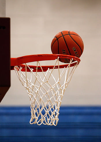 A basketball moment captured as the ball rests on the rim, highlighting the suspense of the game. HD phone wallpaper