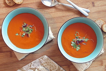Two bowls of vibrant tomato soup garnished with fresh microgreens on a wooden table. HD wallpaper