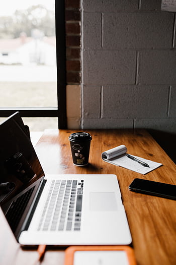 Modern office desk setup with laptop, coffee cup, and notepad by window. HD phone wallpaper