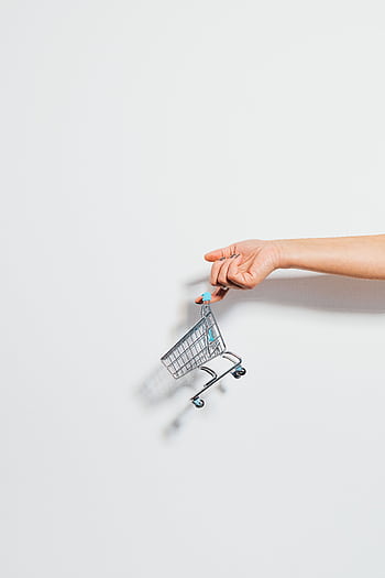 A hand holding a miniature shopping cart against a clean white background, emphasizing simplicity. HD phone wallpaper