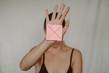 A woman holding an open palm with a pink note showing a cross, symbolizing rejection. HD wallpaper
