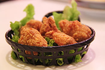 Close-up of crispy fried chicken served in a black basket with fresh lettuce, highlighting food texture. HD wallpaper