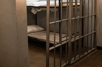 A prison cell featuring a metal bunk bed and striped sheets. HD wallpaper