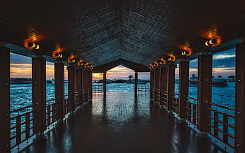 A wooden pier with illuminated lights overlooking a tranquil ocean at sunset, ideal for travel and nature themes. HD wallpaper