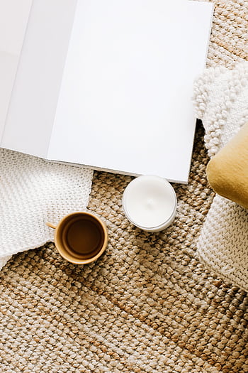 A cozy workspace featuring a blank notebook, coffee mug, and candle on a woven mat. HD phone wallpaper