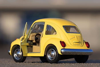Detailed close-up of a yellow miniature Volkswagen Beetle toy car on pavement. HD wallpaper