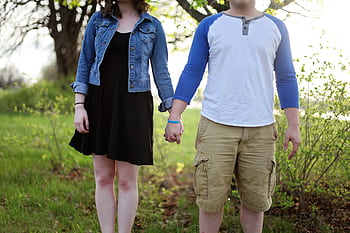 A young couple holding hands outdoors in a park, enjoying a sunny day. HD wallpaper