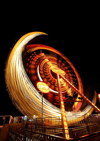 A vibrant long exposure capturing the motion and lights of a Ferris wheel at night. HD phone wallpaper