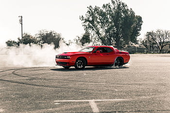 A vibrant red muscle car performing a drift, creating smoke on an open asphalt area in Sacramento, CA. HD wallpaper