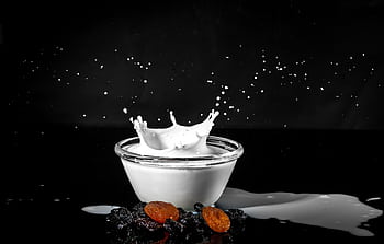Dramatic milk splash in glass bowl with raisins and apricots on black background. HD wallpaper