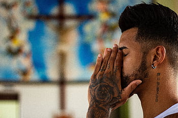A man with tattoos prays inside a church, capturing a moment of reflection and spirituality. HD wallpaper