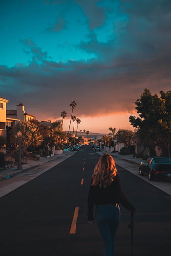 Woman walking on a Los Angeles street during a vibrant sunset with palm trees lining the road. HD phone wallpaper