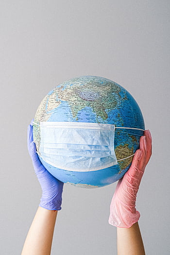 Hands in gloves holding a globe with a mask, symbolizing global health and pandemic protection. HD phone wallpaper