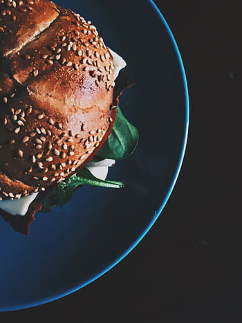 Delicious close-up of a gourmet sandwich with sesame seed bun and spinach on a plate. HD phone wallpaper