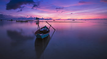 A tranquil sunrise over a tropical ocean with a solitary boat reflecting peaceful hues. HD wallpaper