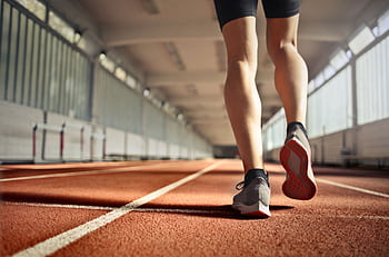 Low-angle view of an athlete in motion on an indoor track, ready to sprint. HD wallpaper
