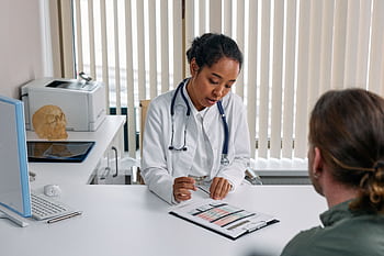 A doctor consulting with a patient in an office, discussing a medical chart. HD wallpaper