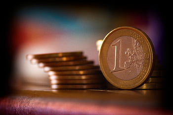A close-up shot of stacked euro coins with a blurred colorful background, representing financial concepts. HD wallpaper